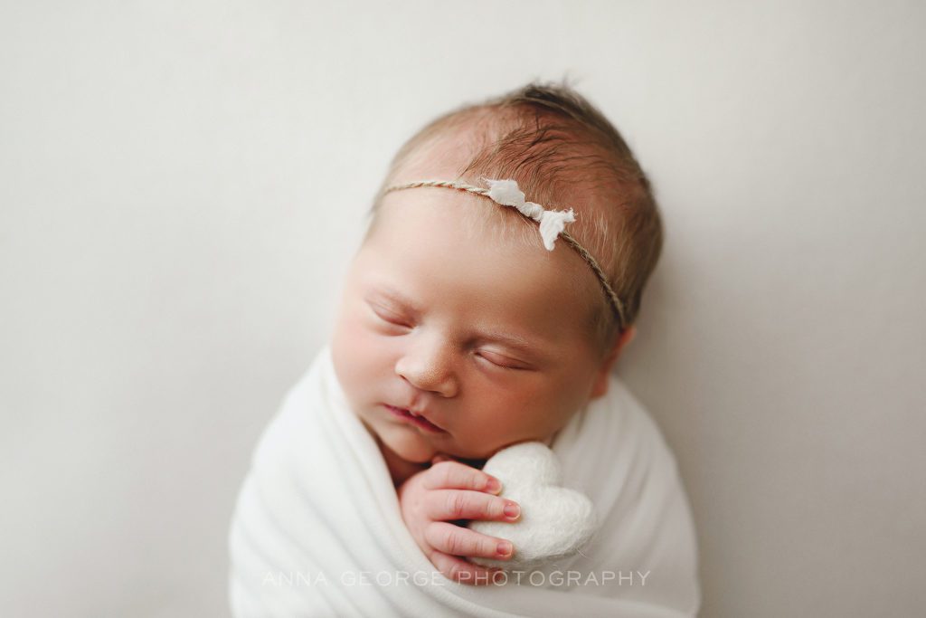 photo of newborn baby holding a felt heart on white background