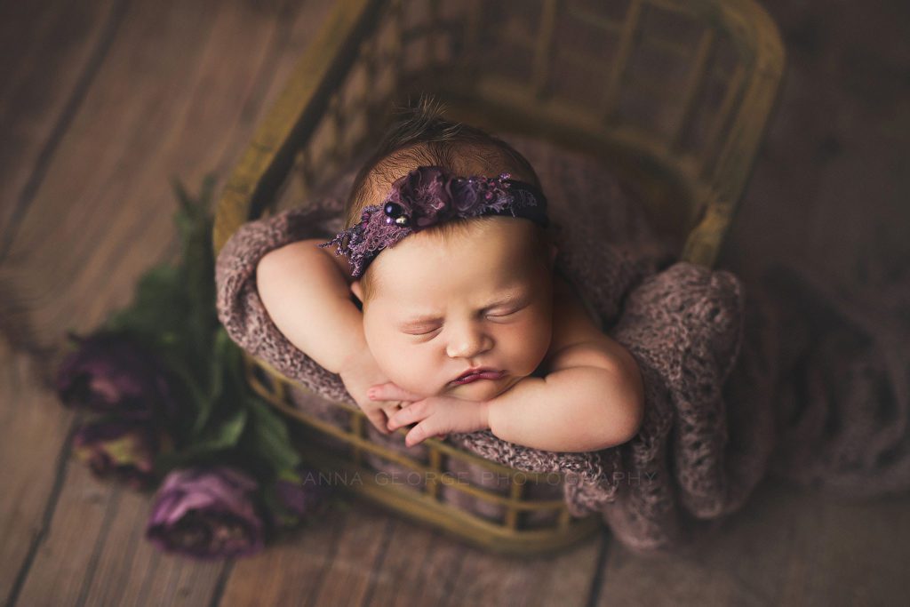 newborn baby girl posed in a basket with flowers