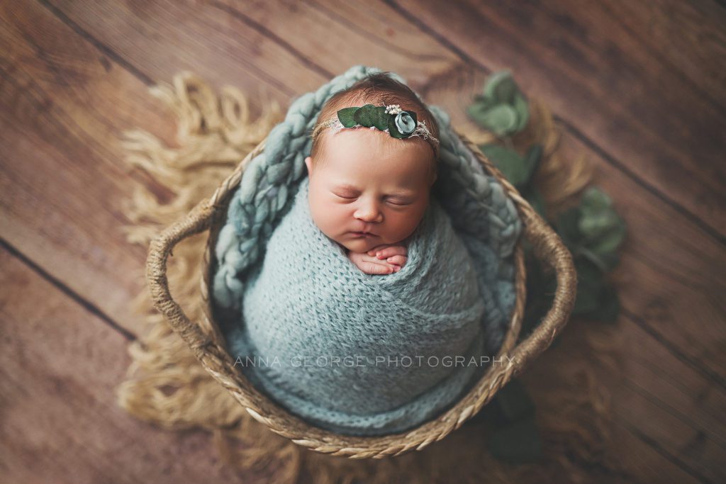 newborn girl wrapped in blue sleeping in a basket