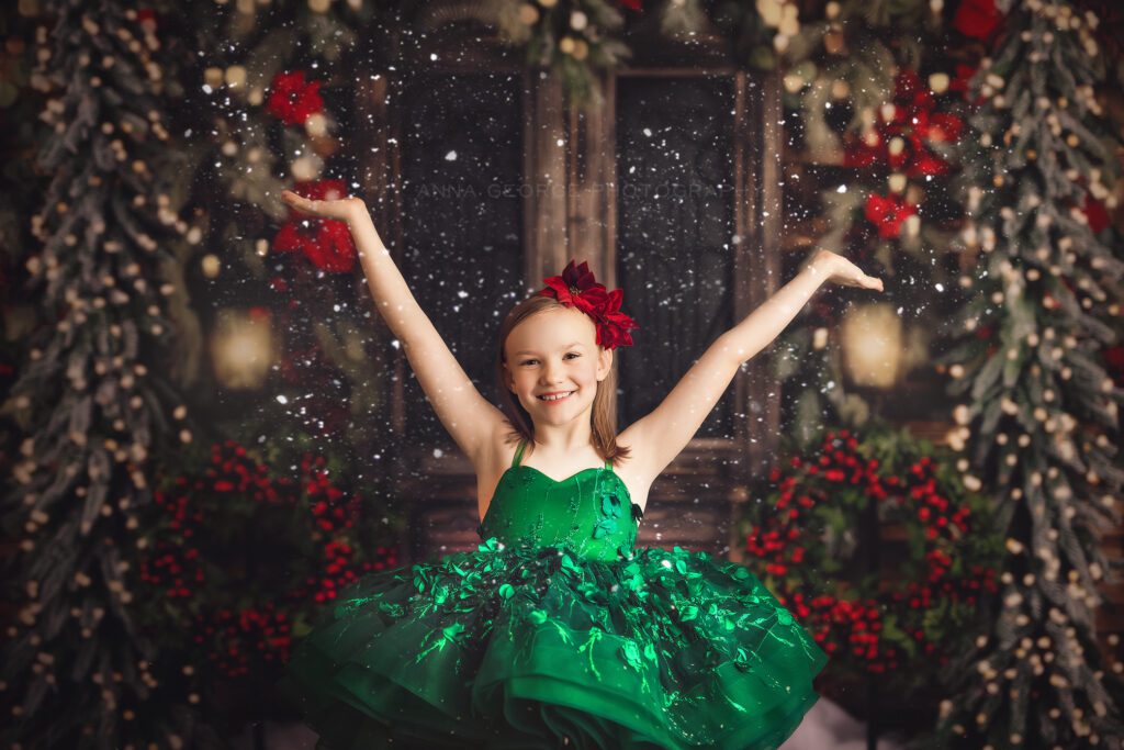 girl in fancy green dress throwing snow up on a christmas backdrop, mini photo session in madison WI studio